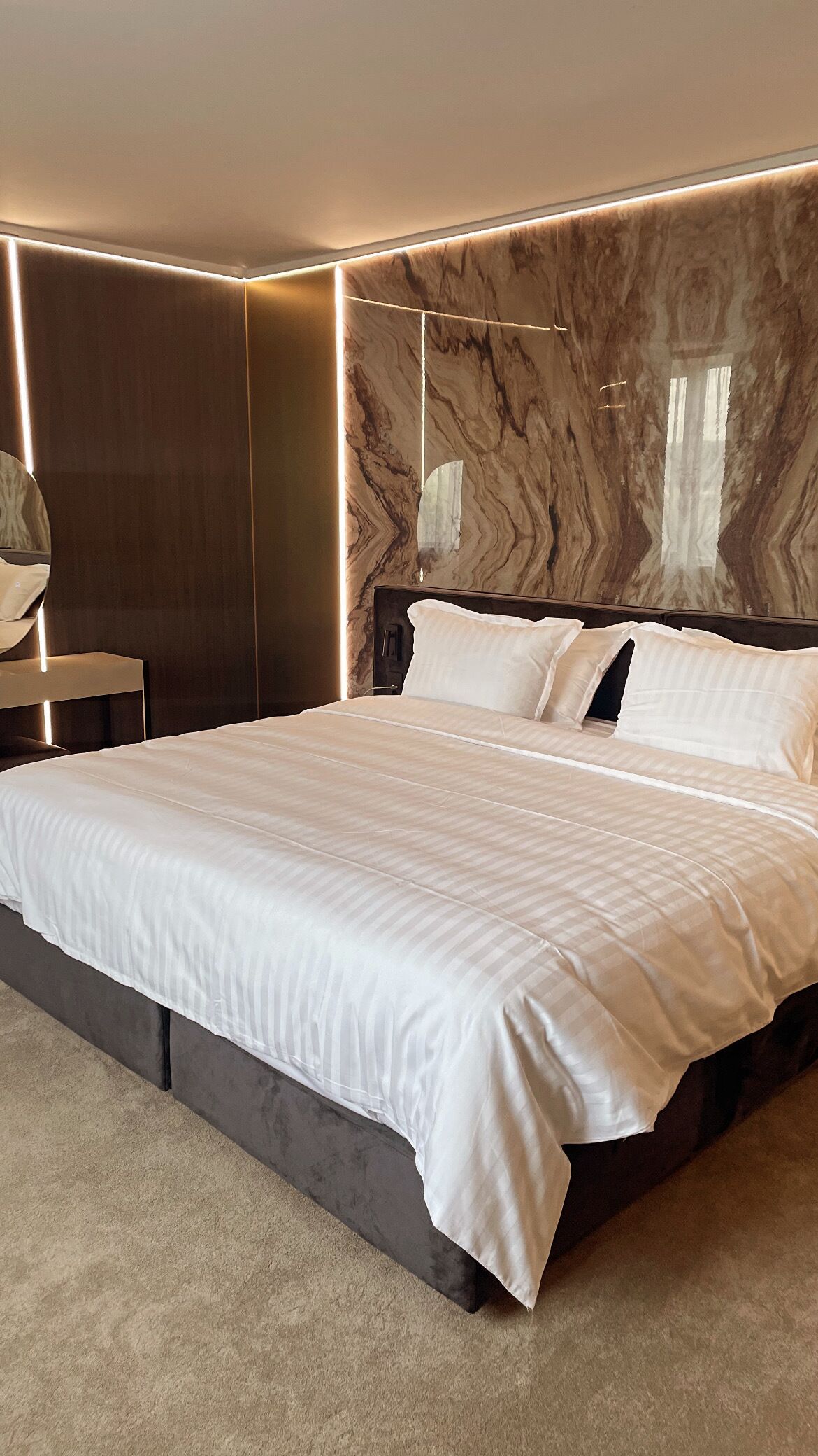 Een moderne slaapkamer met een groot bed, een donker hoofdbord en een marmeren wand.