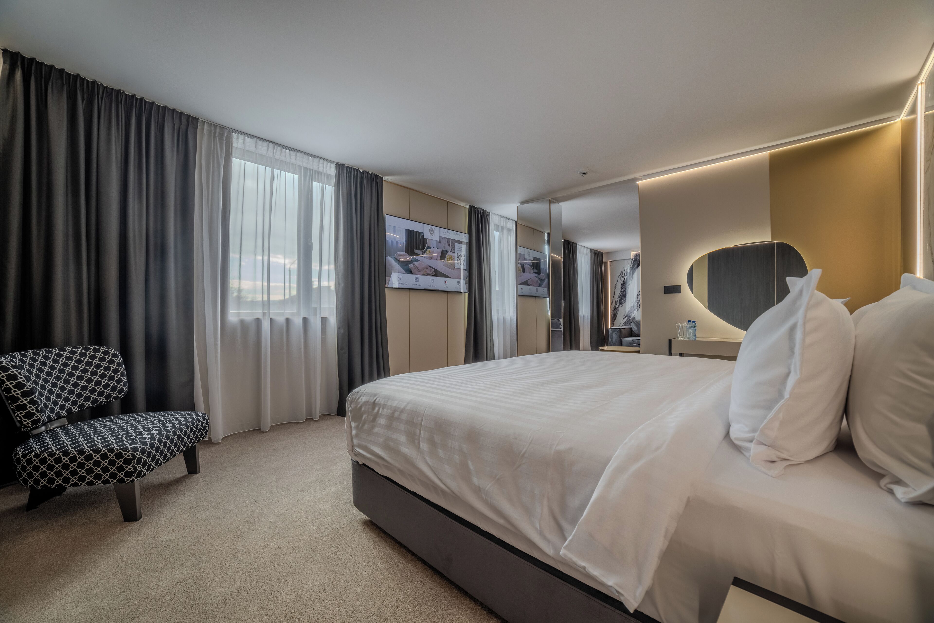 Habitación de hotel con una cama grande, una silla, un espejo y un televisor en la pared.