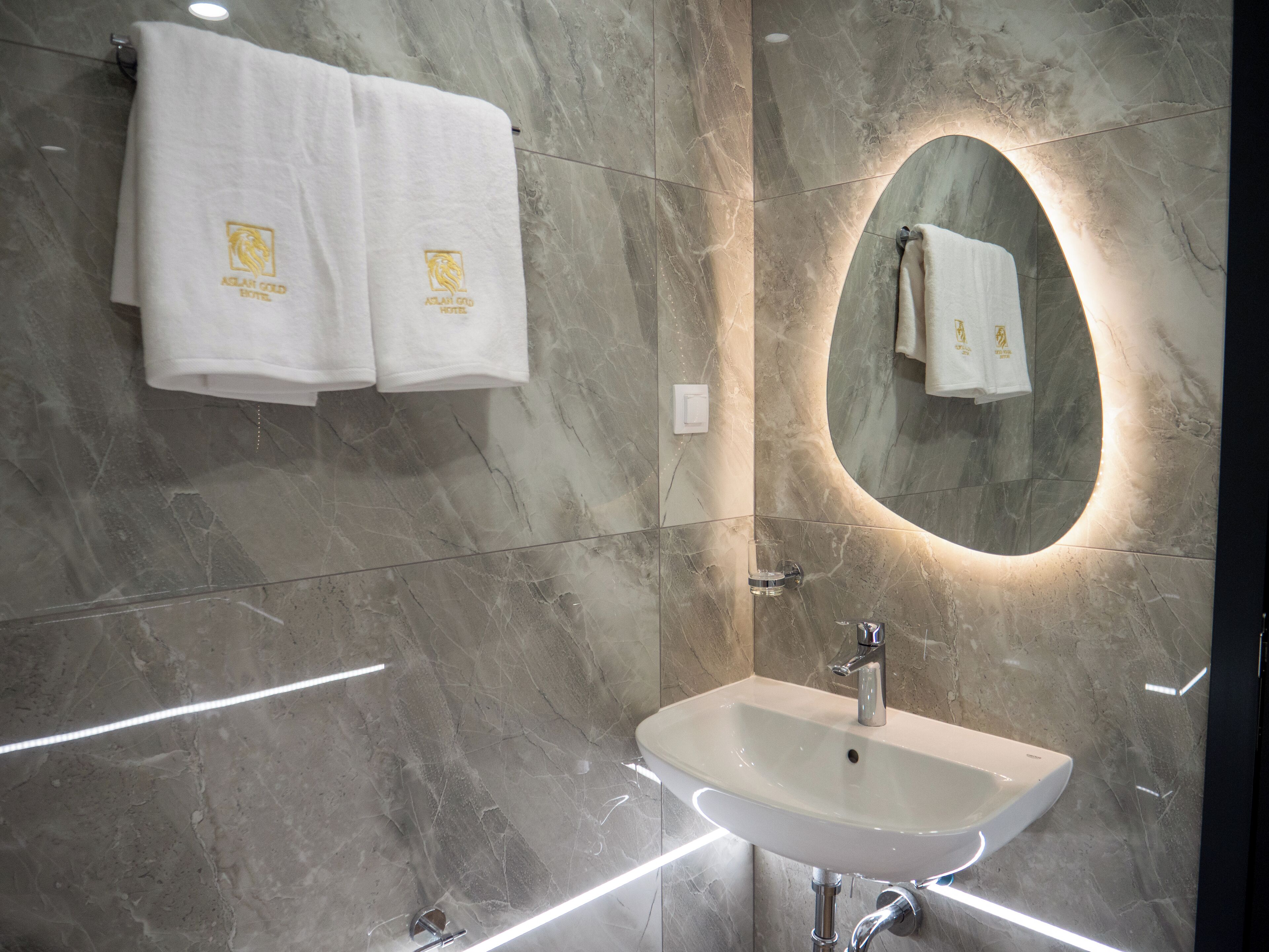 A modern bathroom with a marble floor, a white sink, and two towels hanging on the wall.
