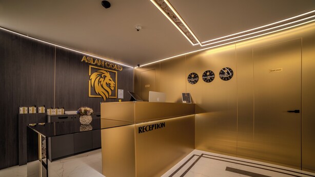 A reception area with a gold counter, a lion logo, and clocks on the wall. - Aslan Gold Hotel (Varna)