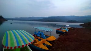 A lakeside view with boats and a striped umbrella. - OMKAR AGRO TOURISM AND RESORT (Mahabaleshwar)