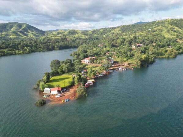 A lakeside property with a dock, boats, and a small building. - OMKAR AGRO TOURISM AND RESORT (Mahabaleshwar)