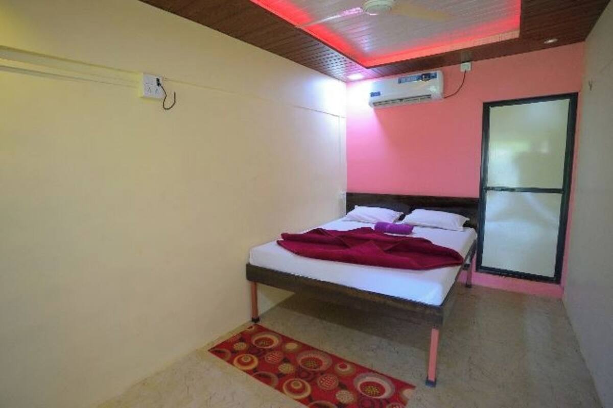 A small, single-bed room with a wooden ceiling, a red patterned rug, and a white wall with a window.