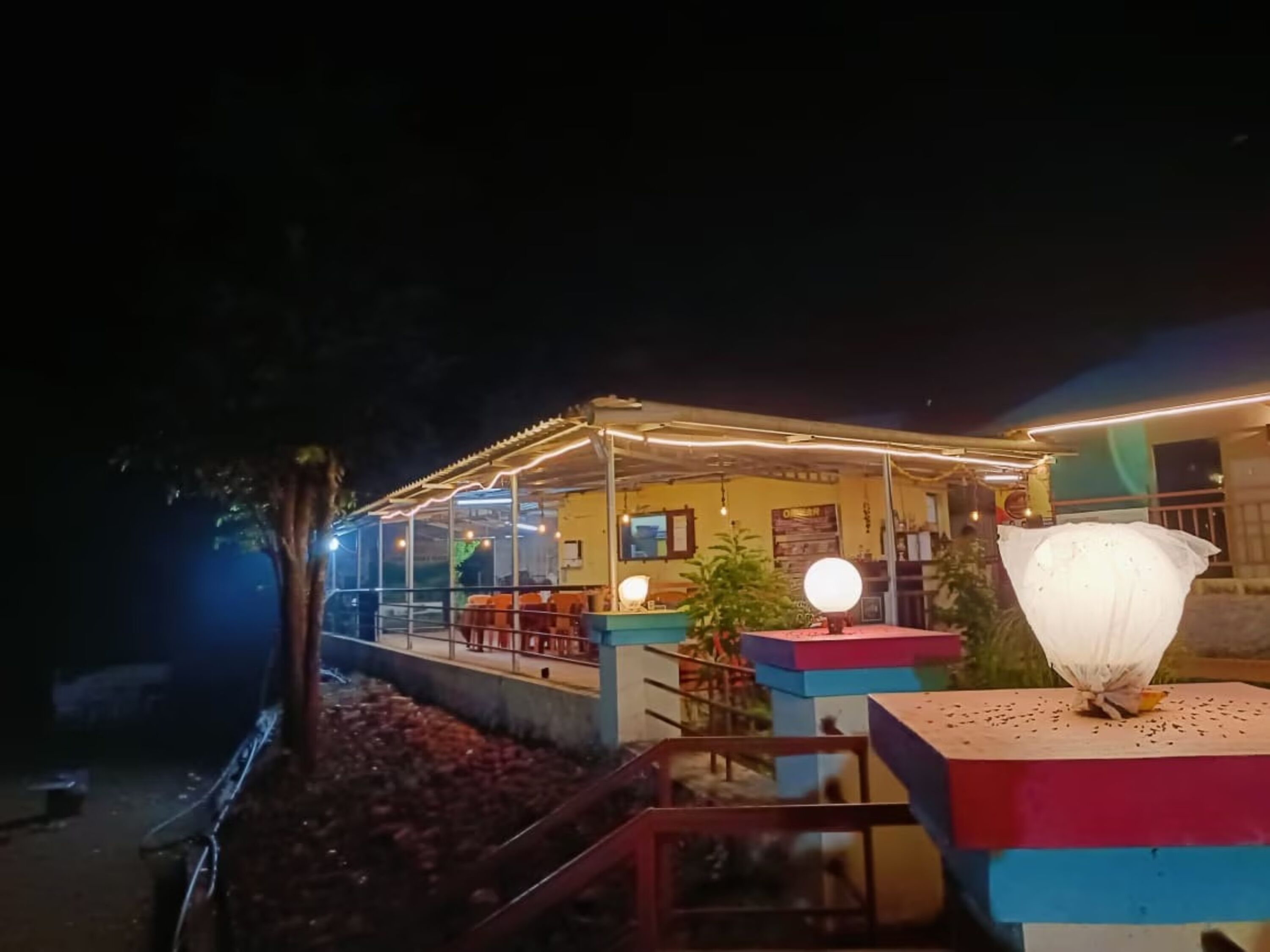 Een overdekt terras met tafels, stoelen, een lamp en een decoratieve plant.