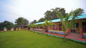 A building with a flat roof, multiple windows, and a grassy courtyard. - OMKAR AGRO TOURISM AND RESORT (Mahabaleshwar)