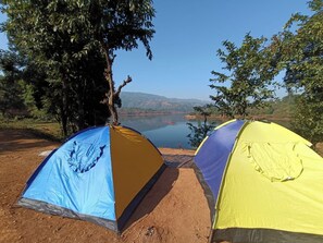 Two tents set up on a dirt ground with a lake and hills in the background. - OMKAR AGRO TOURISM AND RESORT (Mahabaleshwar)
