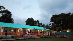 A building with a green roof, a covered outdoor area with seating, and a grassy lawn. - OMKAR AGRO TOURISM AND RESORT (Mahabaleshwar)