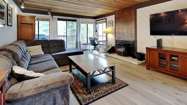 A cozy living room with a wooden ceiling, a large TV, a fireplace, and a comfortable seating area. - Slopeside Condo with Fireplace (Mammoth Lakes)