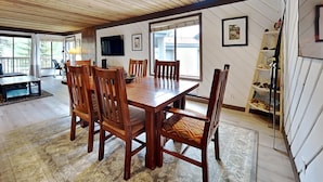 A dining area with a wooden table and chairs, a television on the wall, and a large window providing natural light. - Slopeside Condo with Fireplace (Mammoth Lakes)
