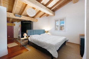 Ein Schlafzimmer mit Bett, Nachttischen, einer Lampe, einem Fenster und Holzbalken an der Decke.