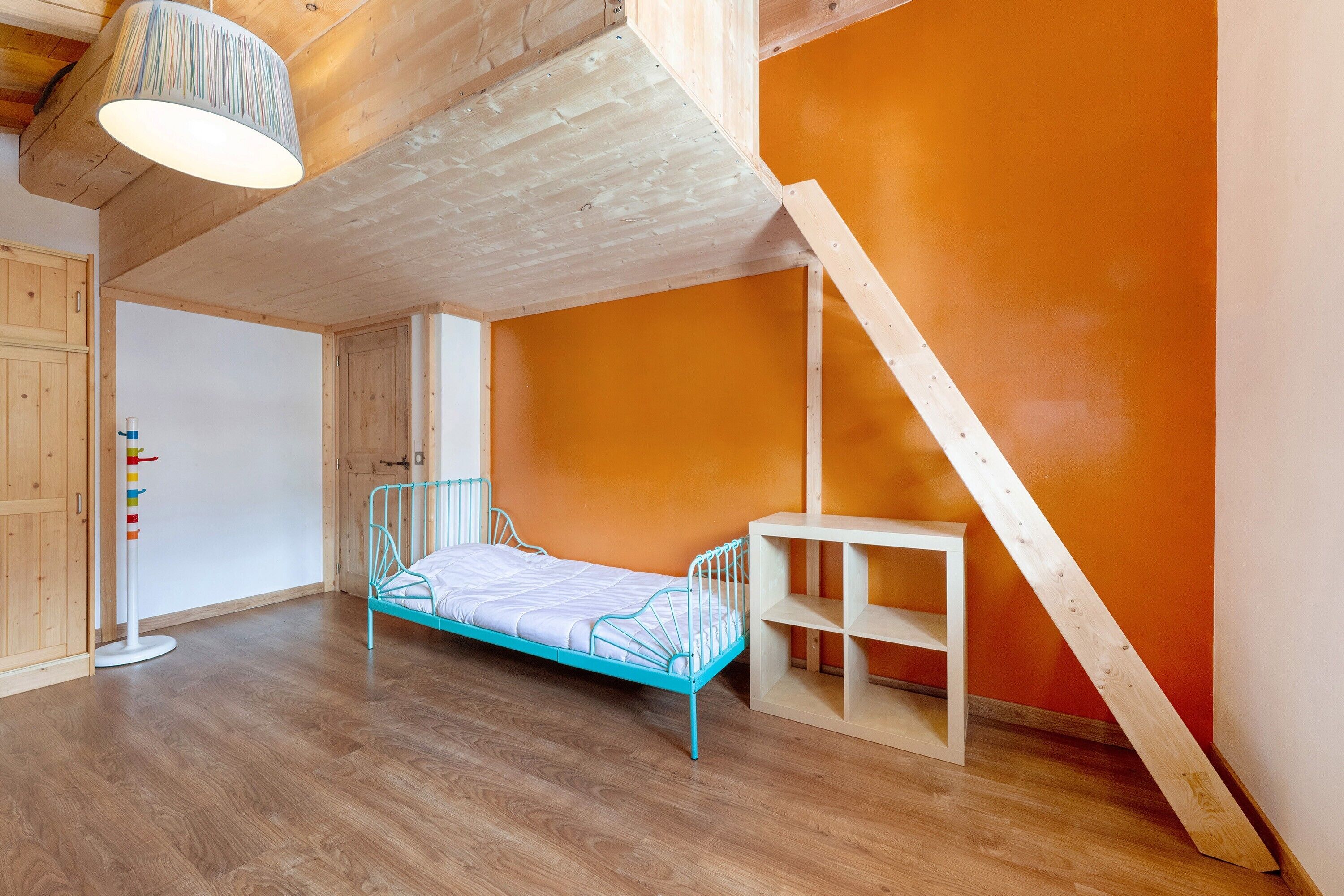 A room with a wooden ceiling, a blue metal bed, a white shelf, and a wooden staircase.