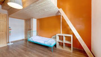 A room with a wooden ceiling, a blue metal bed, a white shelf, and a wooden staircase.