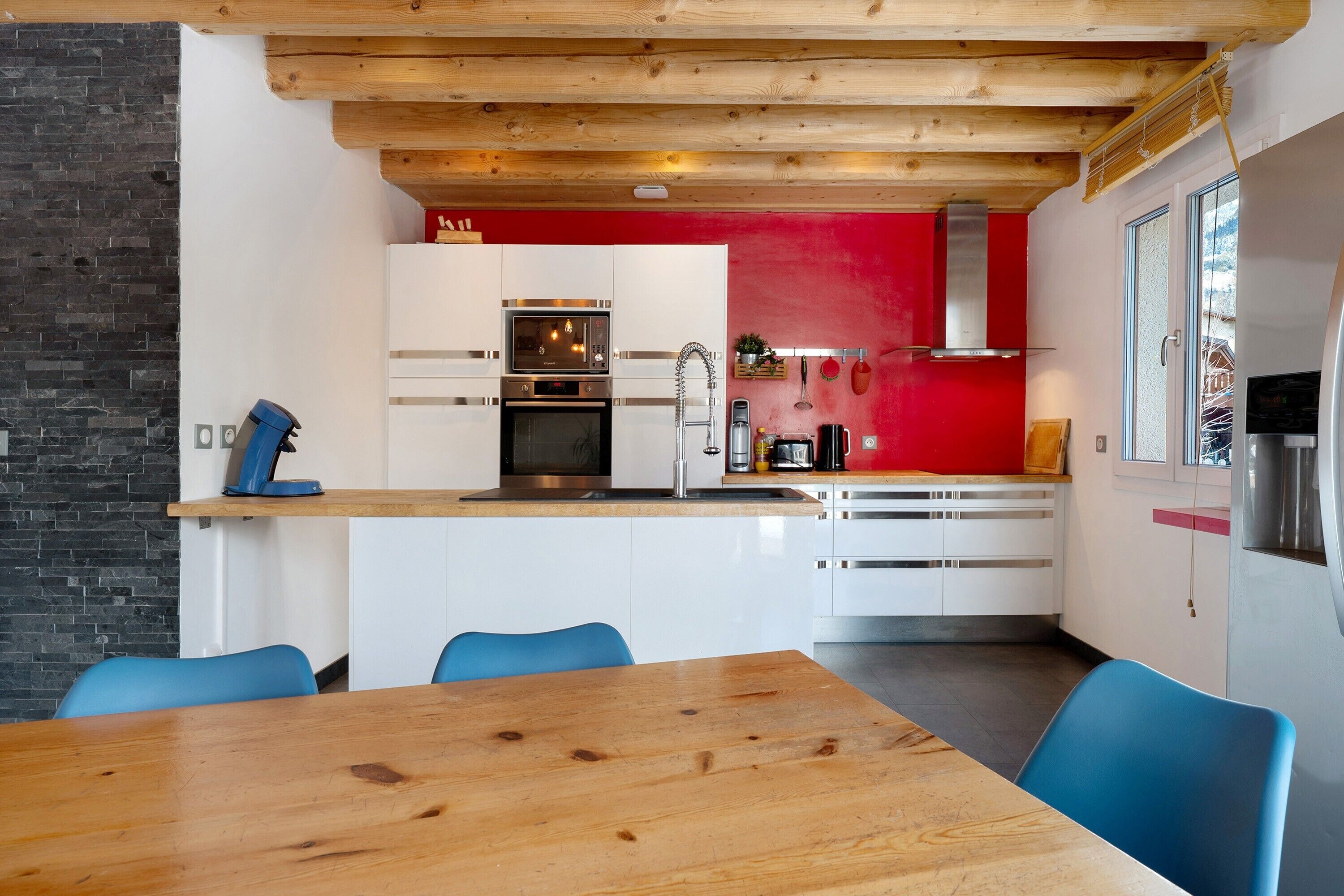 Una cocina moderna con armarios blancos, una pared de acento roja y techo de madera.