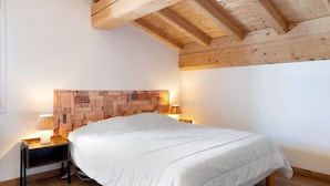 Een slaapkamer met een houten plafond, een hoofdbord met een baksteenpatroon, een wit bed en twee bedlampjes.
