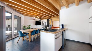 Een moderne keuken met een centraal eiland, houten balken in het plafond, een inbouw vaatwasser en een groot raam met uitzicht op het terras.