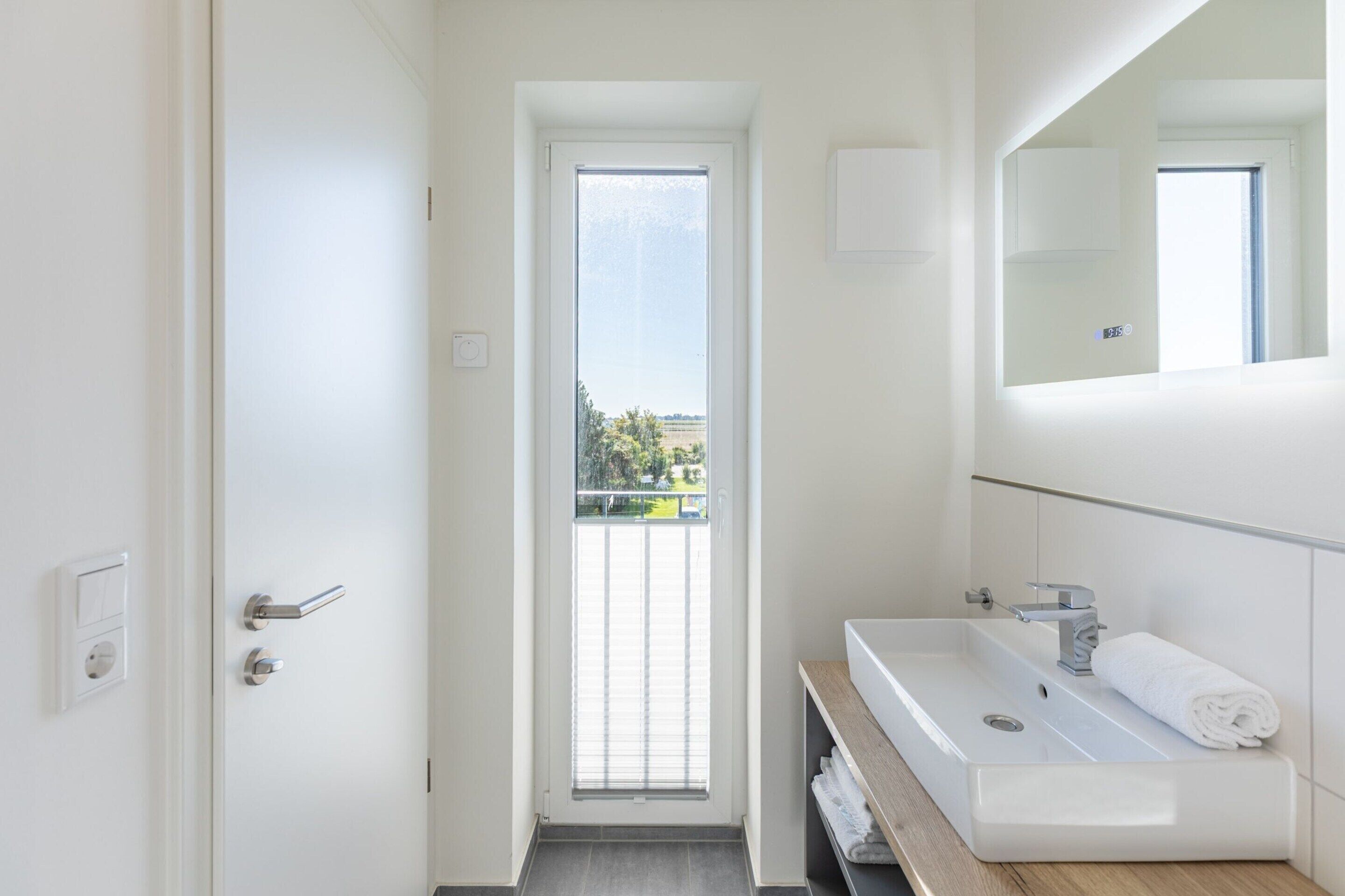 A modern bathroom with a white sink, a mirror, and a door leading to a balcony.