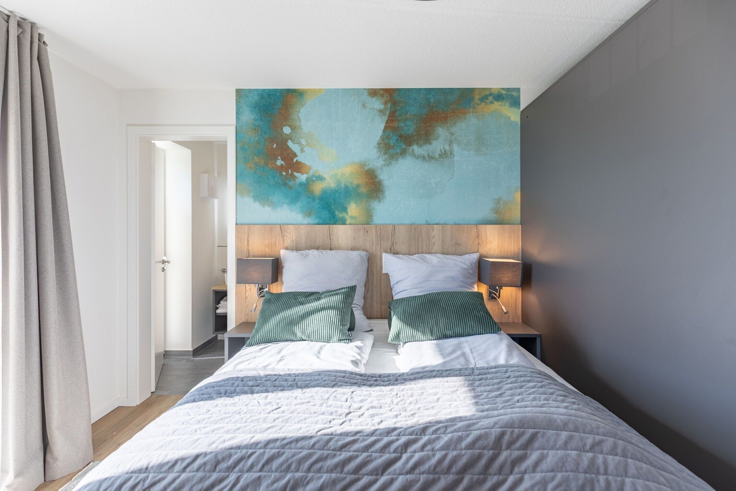 A modern bedroom with a large bed, two bedside tables with lamps, and a large abstract painting on the wall.