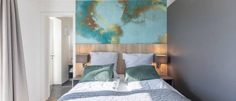 A modern bedroom with a large bed, two bedside tables with lamps, and a large abstract painting on the wall.