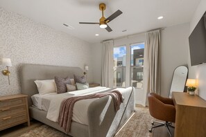 A modern bedroom with a bed, bedside tables, a desk, a chair, a ceiling fan, and a large window. - Sandy Cheeks 6 Bedroom Townhouse (St. George)
