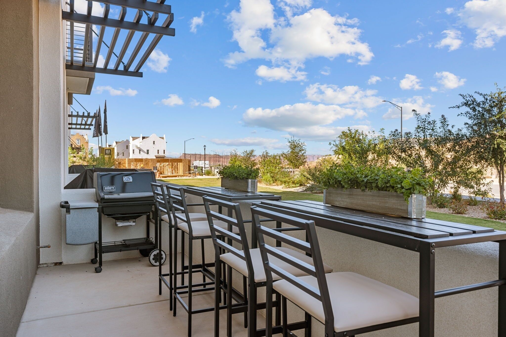 An outdoor patio with a grill, bar stools, and a view of the neighborhood.