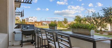 An outdoor patio with a grill, bar stools, and a view of the neighborhood.