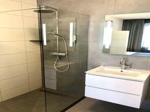 Ein modernes Badezimmer mit einer Duschkabine, einem weißen Waschbecken und einem Spiegel darüber.