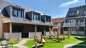 En modern bostadsbyggnad med ett takförsett utomhusområde som har träbänkar och en stenlagd gångväg.