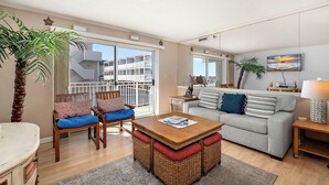 Un salón con sofá, sillas, una mesa y un balcón con vistas a un edificio.