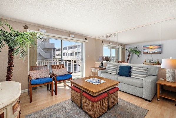 A living room with a sofa, chairs, a table, and a balcony with a view of a building. - Sand Pointe 101 - great views from the side of this oceanfront bldg. Great mid town location, 3 br / 2 baths (Ocean City)