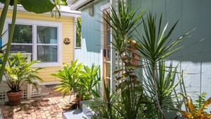 A courtyard with potted plants, a white fence, and a yellow building with a window. - Old Town Studio Cottage with Full Kitchen, In-Unit Laundry & Shared Pool (Key West)
