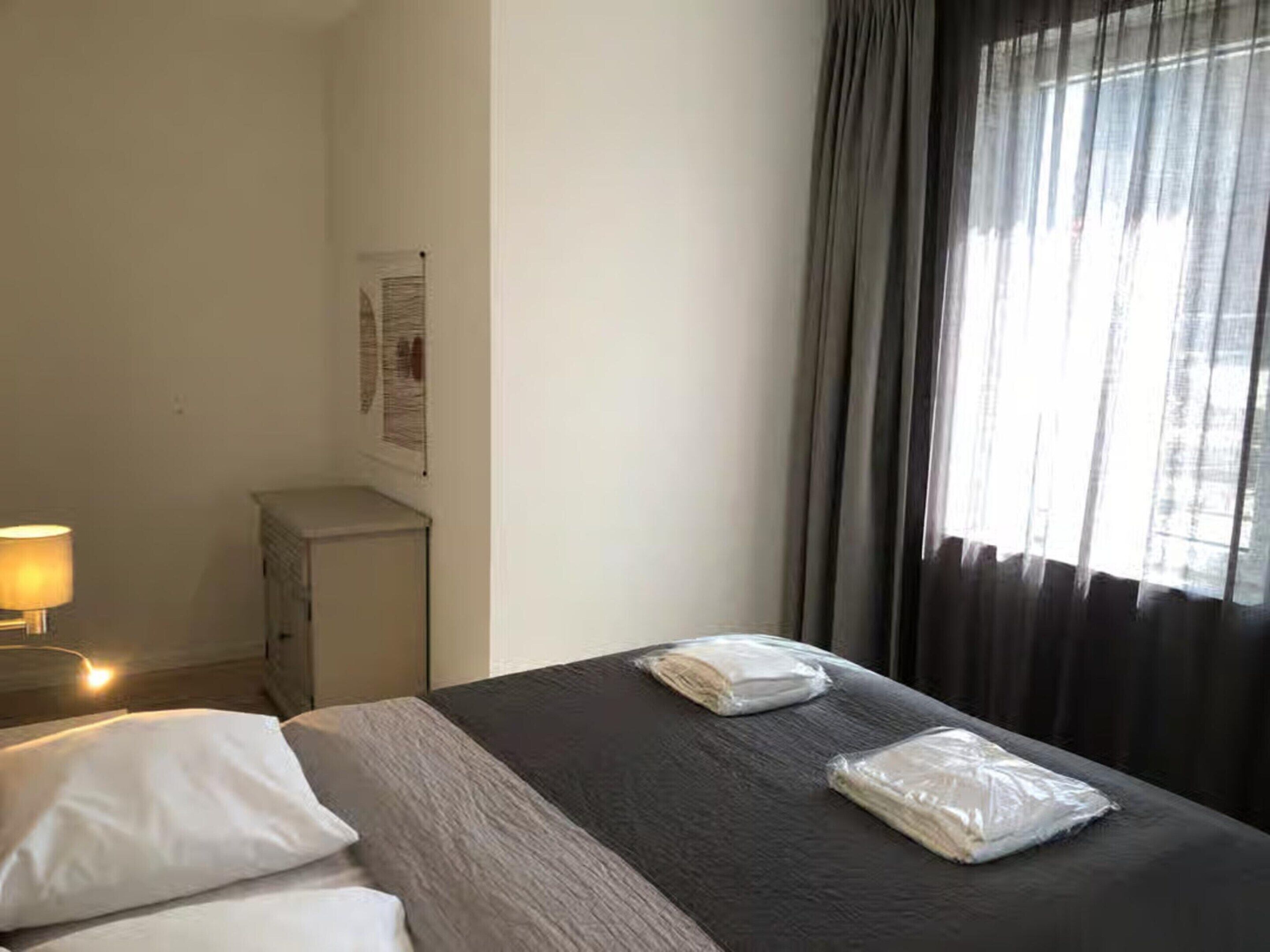 A hotel room with a bed, a nightstand, a lamp, and a window with curtains.