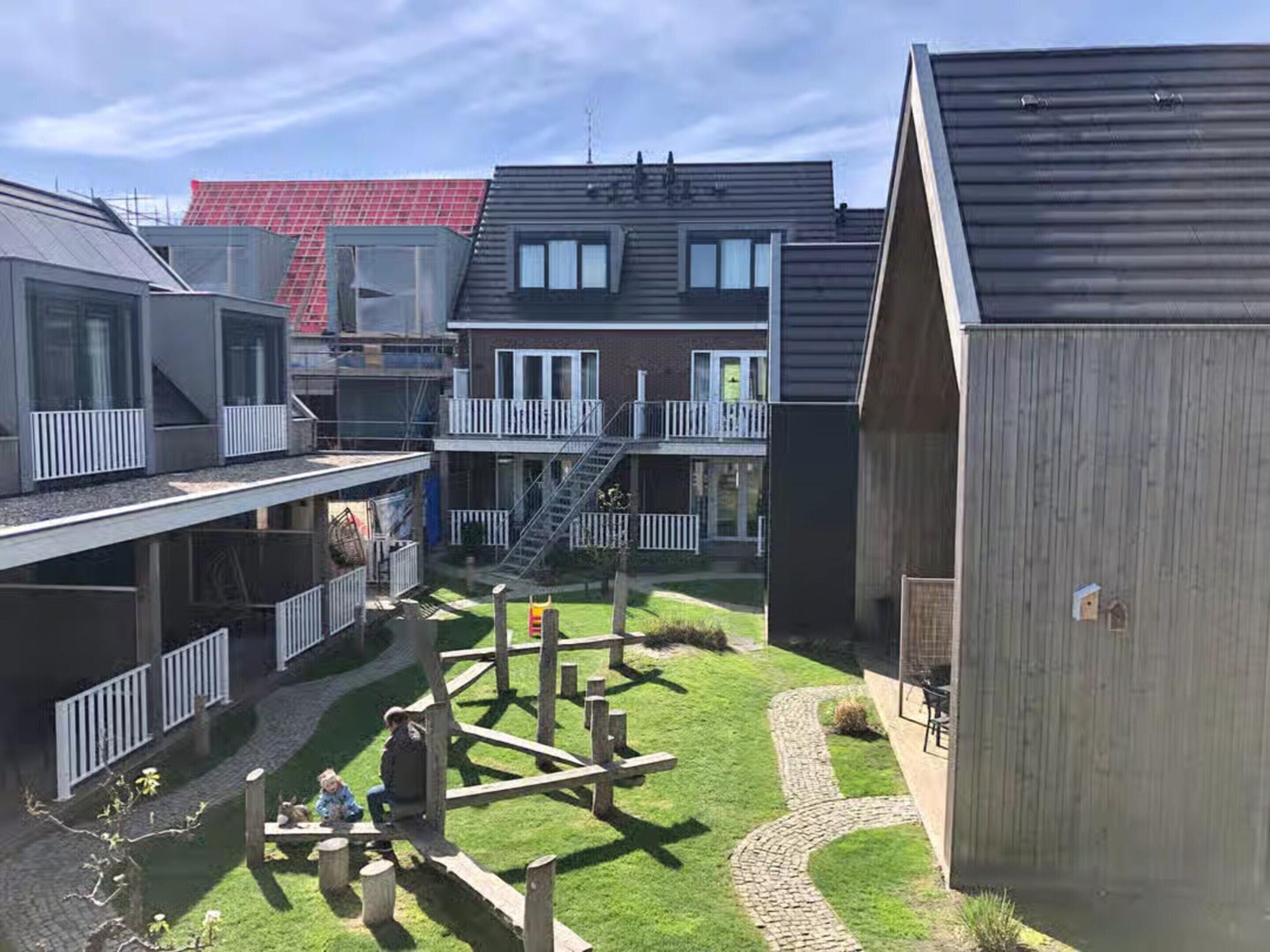 A courtyard with a playground, a building with a balcony, and a wooden structure.