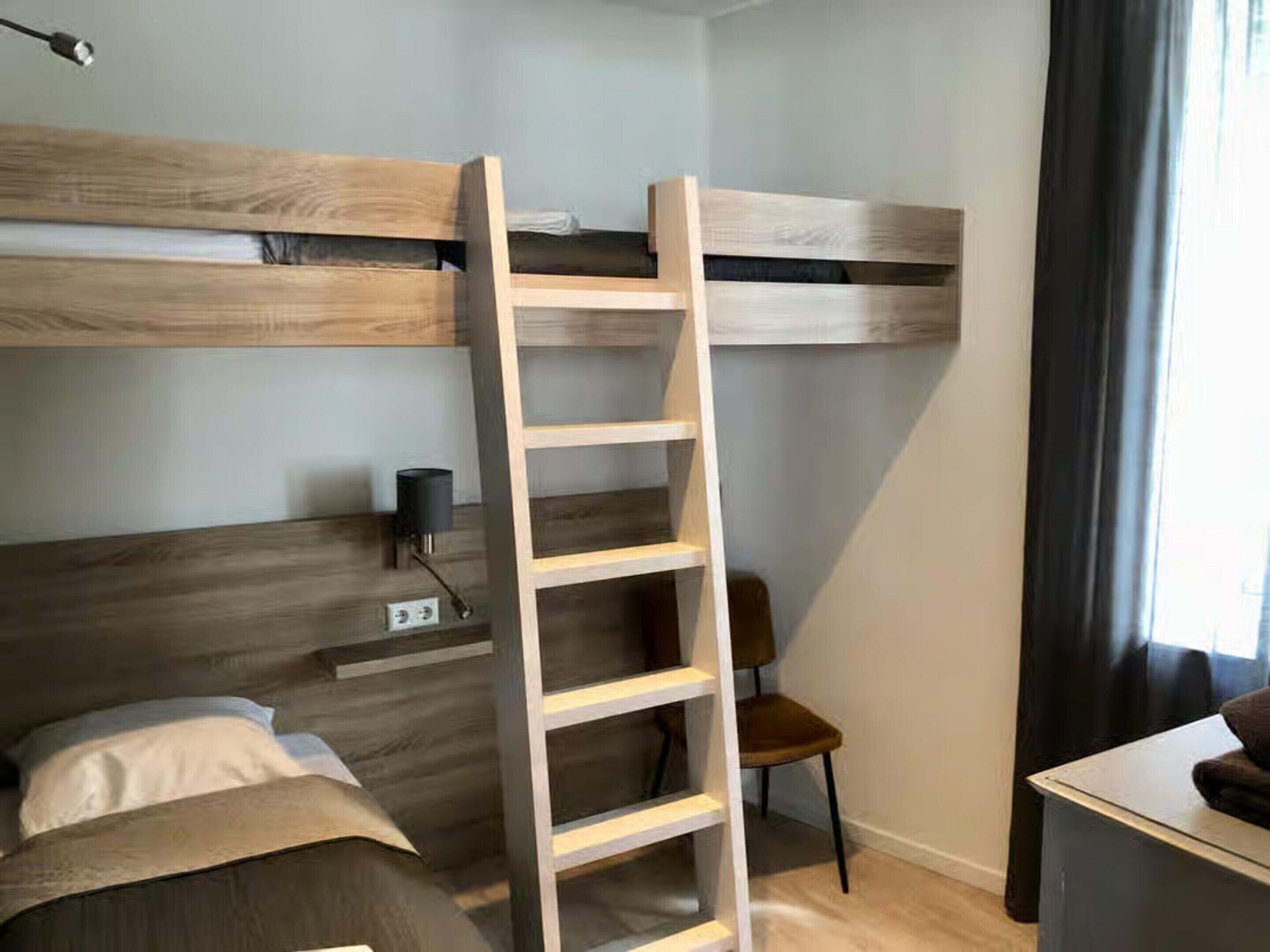 A bedroom with bunk beds, a ladder, a desk, and a chair.