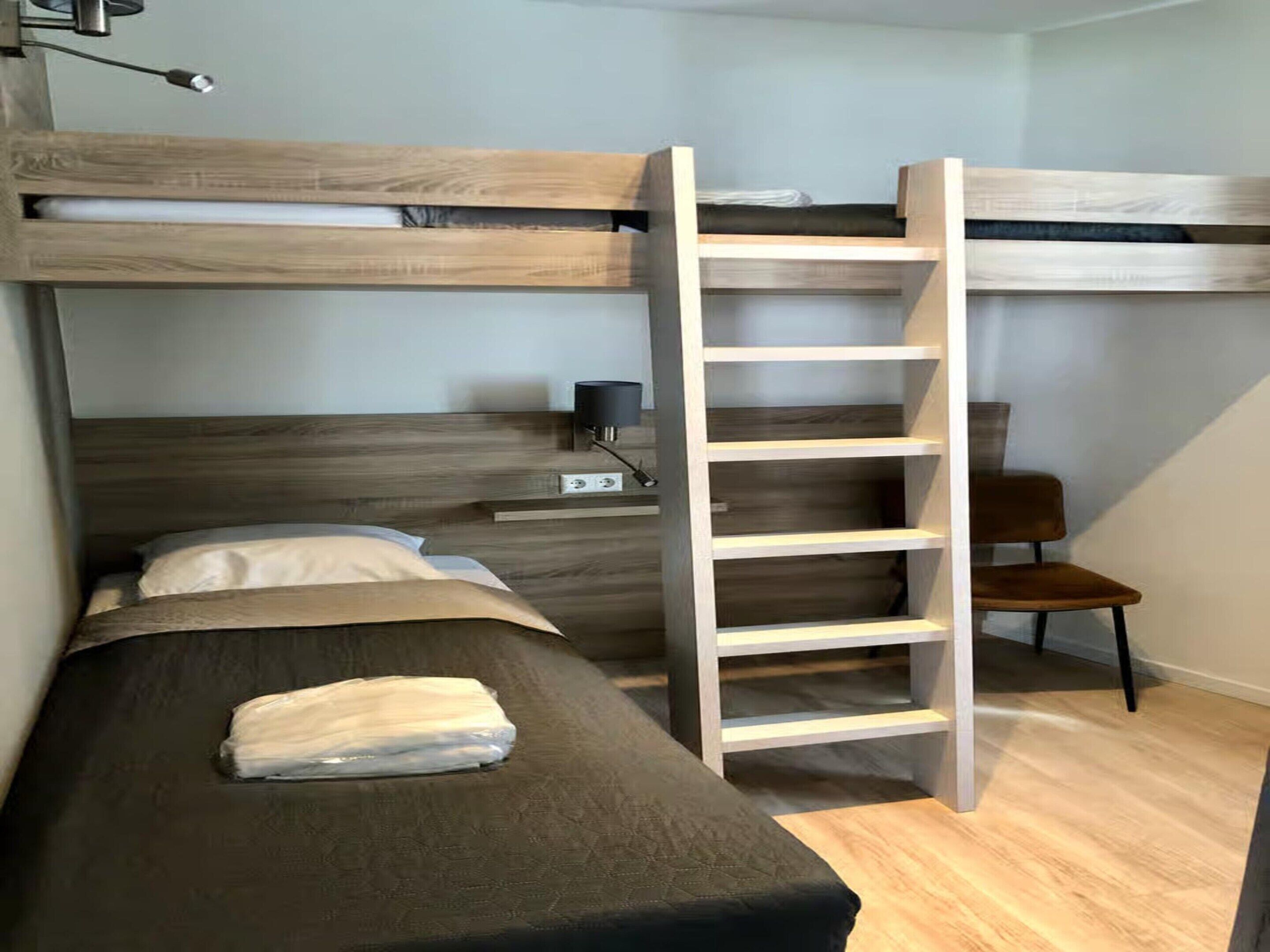 A bunk bed with a ladder, a bedside table, and a chair.