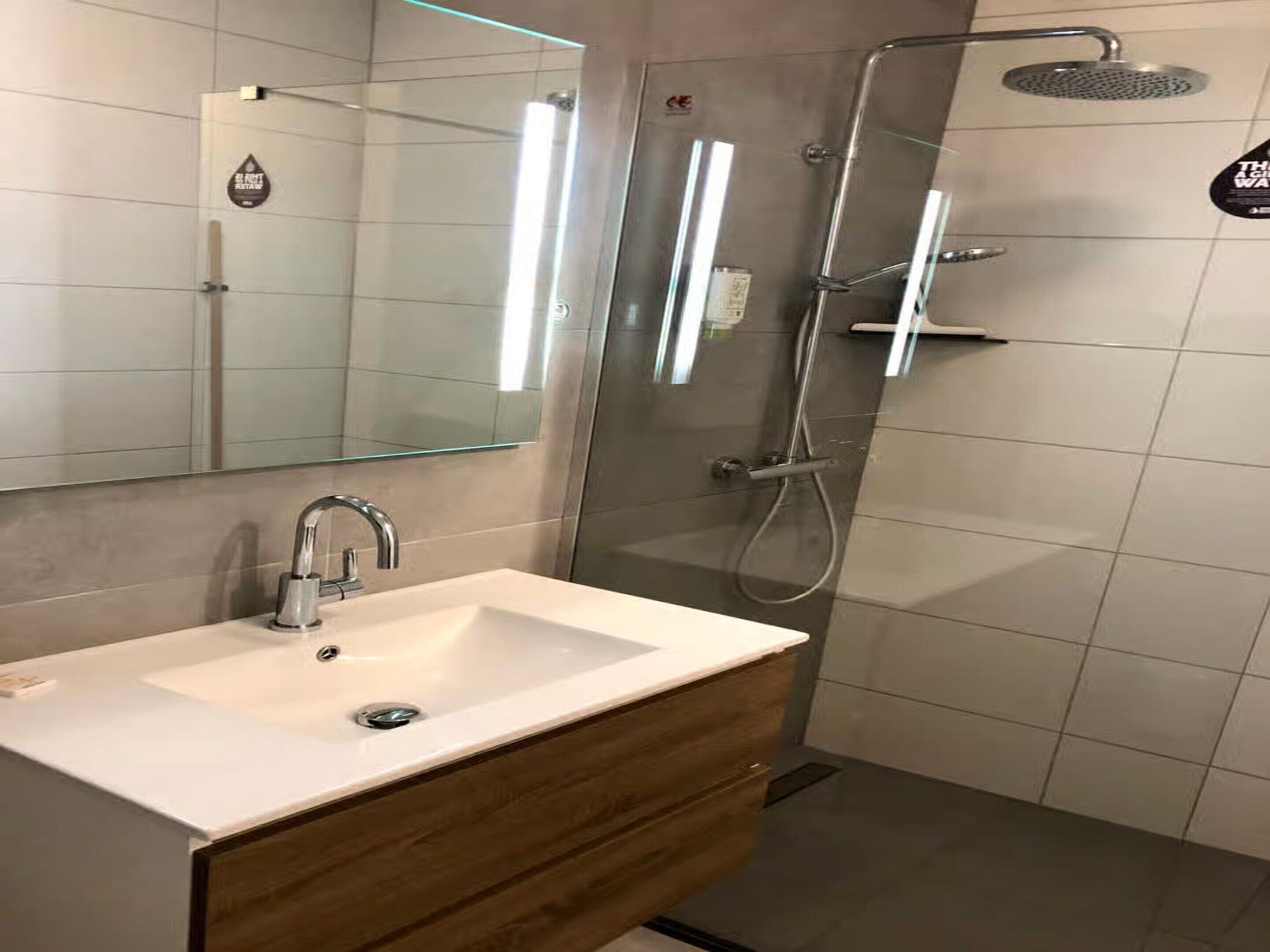 A modern bathroom with a white sink, wooden vanity, and a glass shower enclosure.