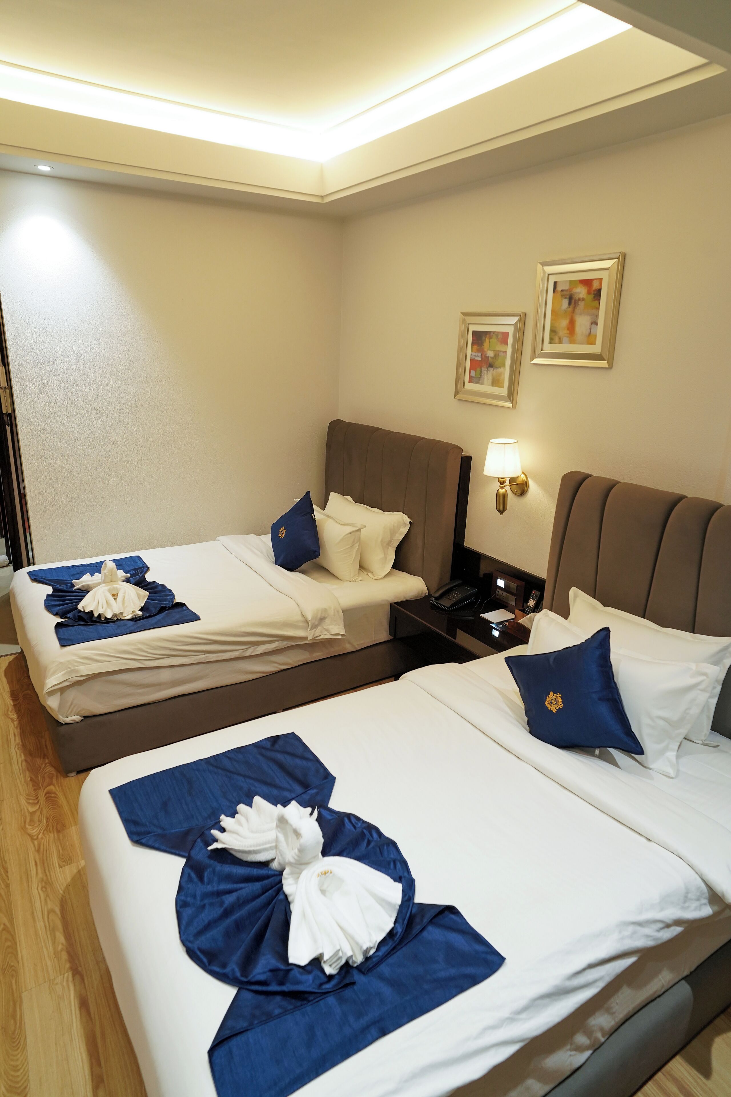 Une chambre d’hôtel avec deux lits, chacun agrémenté de draps blancs et de touches de couleur bleue, une table de chevet avec une lampe et une œuvre d’art accrochée au mur.