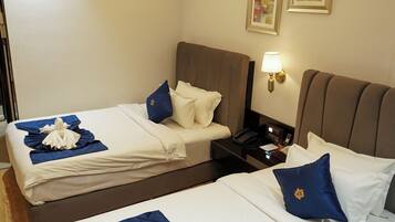Une chambre d’hôtel avec deux lits, chacun agrémenté de draps blancs et de touches de couleur bleue, une table de chevet avec une lampe et une œuvre d’art accrochée au mur.