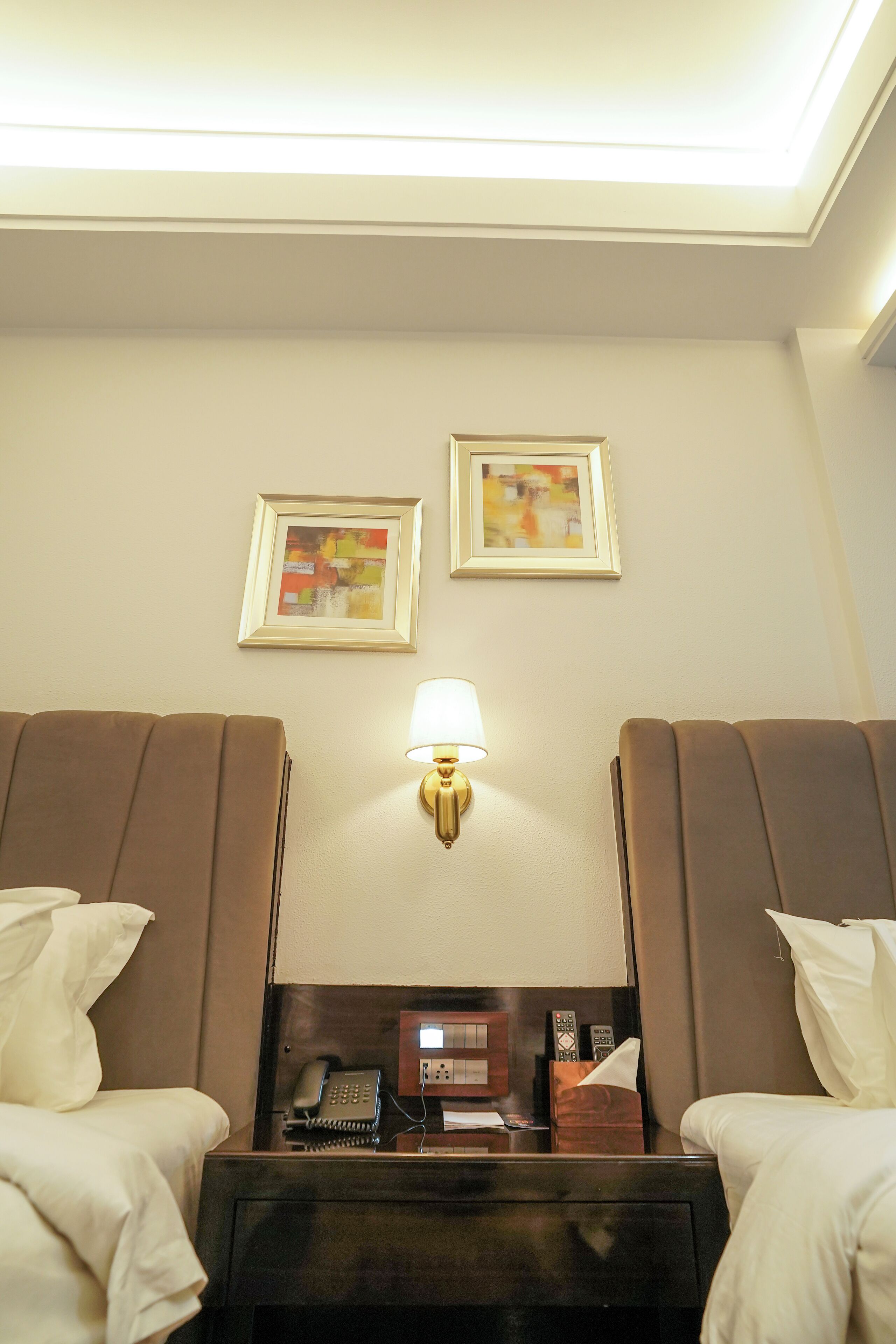 A hotel room with two beds, a nightstand with a phone and remote controls, and wall-mounted artwork.
