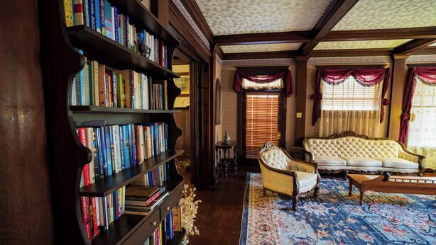 A library with bookshelves, a sofa, and a patterned rug. - Warm, Cozy and Historic (Poplar Bluff)