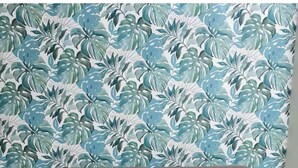 Um sofá cinzento encostado a uma parede com padrão de folhas tropicais. À frente do sofá, uma mesa de centro de vidro com estrutura metálica.