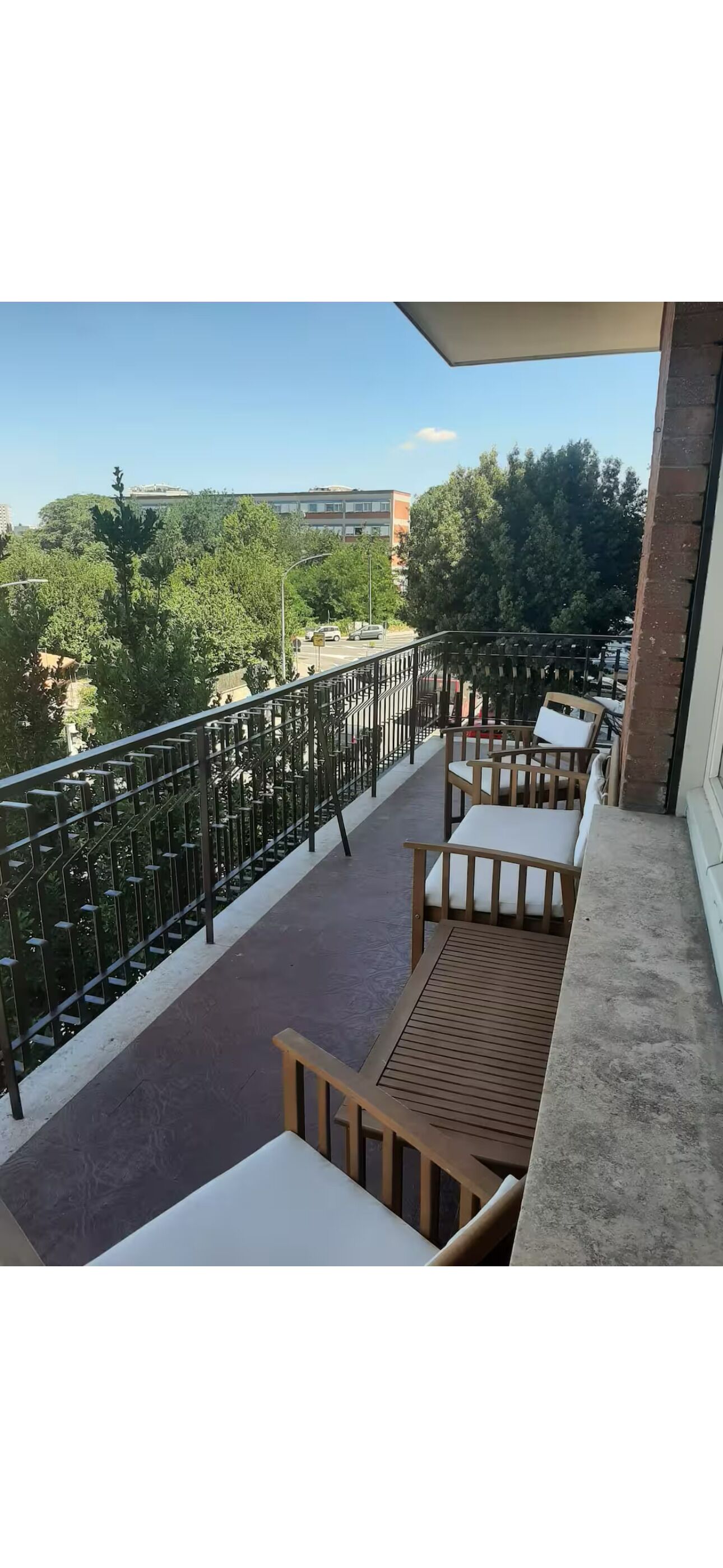 A balcony with a view of trees and buildings, furnished with wooden chairs and a table.