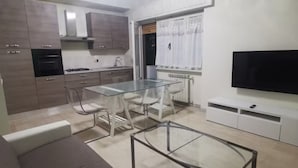 Uma cozinha moderna com eletrodomésticos embutidos, um espaço de refeições com mesa de vidro e uma televisão de tela plana.