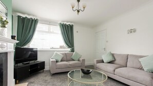 A living room with a TV, two sofas, a glass coffee table, and a fireplace. - Red Courts (Brandon)