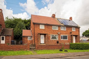 A two-story brick house with a tiled roof, solar panels, and a small front garden. - Toast Stays - The Garnet Rest (Brandon)