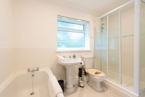 A bathroom with a bathtub, a pedestal sink, a toilet, and a glass-enclosed shower. - Toast Stays - The Garnet Rest (Brandon)