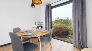 A dining area with a round table, grey chairs, and a view of greenery outside. - Modern House | Garden | Air Conditioning | Close to the Forest (Bielsko-Biała)