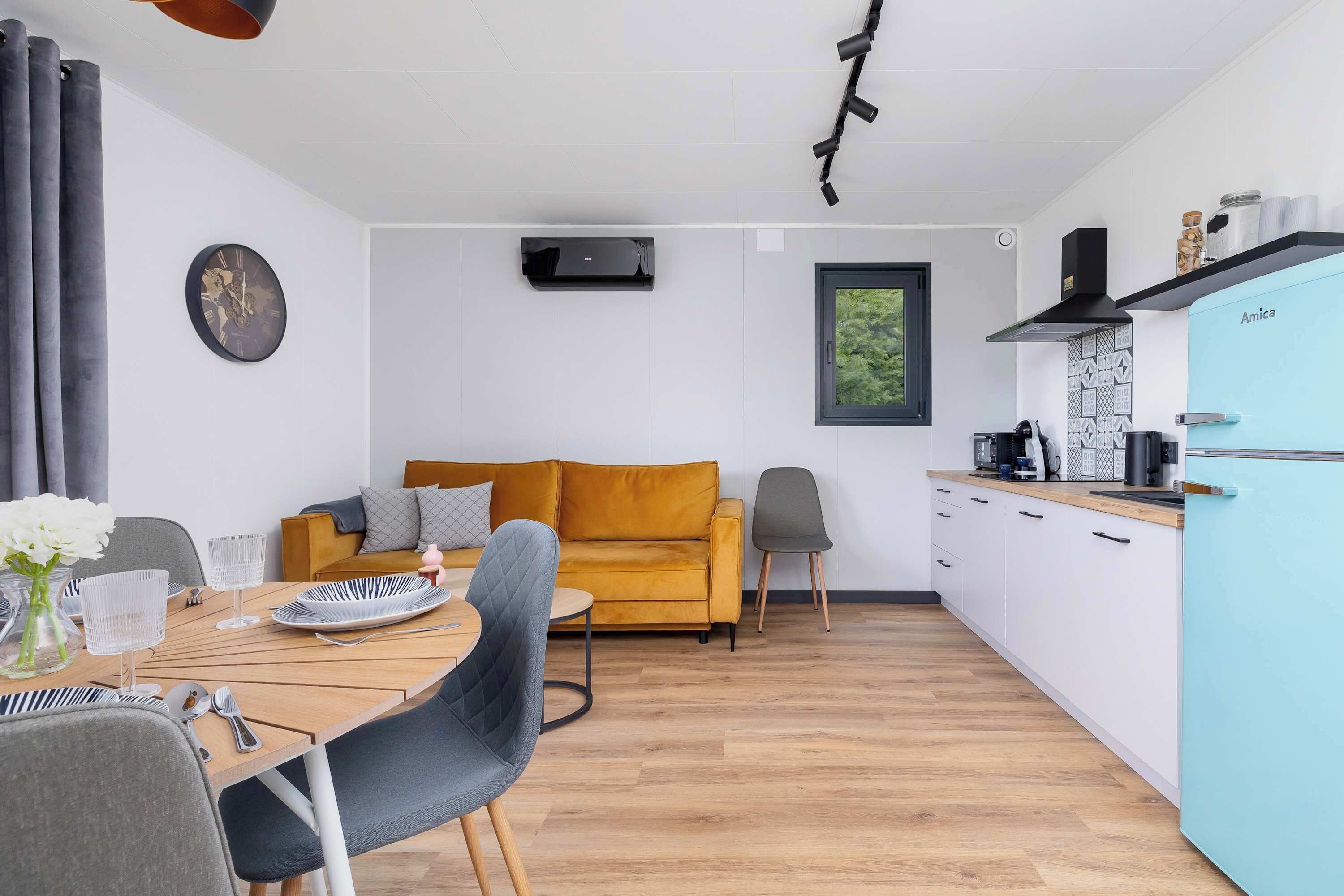Een moderne woonruimte met een eethoek, een bank, een keuken en een klok aan de muur.