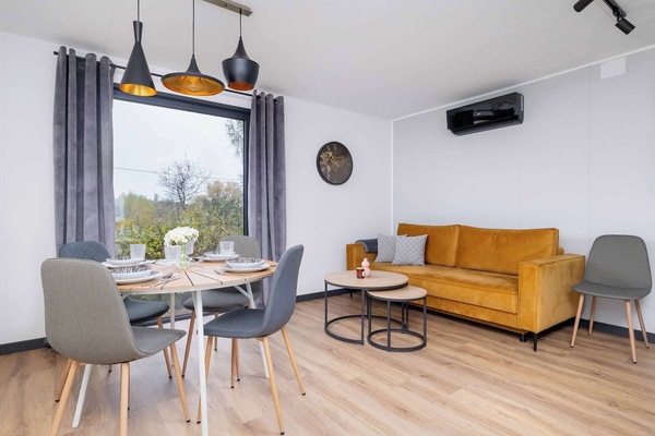 A cozy dining area with a small table set for two, modern chairs, and a wooden sideboard. Natural light enters through a nearby window.