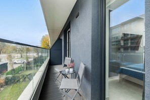 Ein Balkon mit einem Bett, einem Sessel, einem kleinen Tisch und einem Blumentopf.