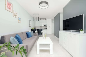 A modern living room with a sofa, coffee table, TV, and kitchen area. - Comfortable Apartment | Sauna, Gym and Parking (Kołobrzeg)